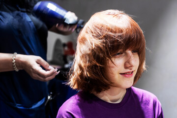 teenage girl with red hair in the hairdresser's on styling her hair. Everyday life, fashion and...