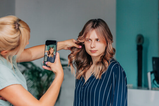 Hairdresser taking picture of young client in salon