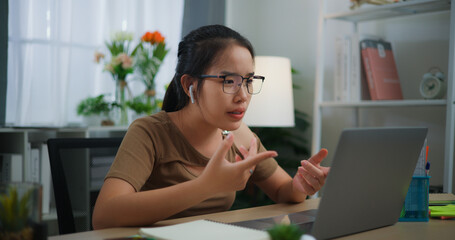 Happy young Asian woman wearing earphone doing video conference on a laptop