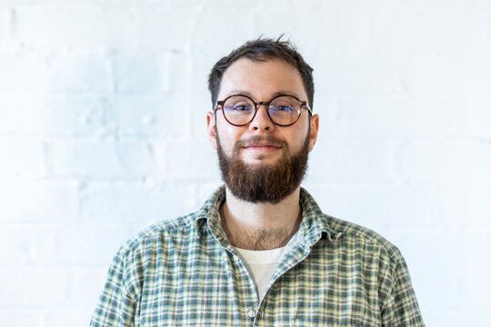 Smiling Young Businessman Wearing Eyeglasses In Front Of White Wall