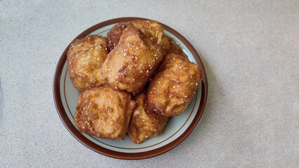 Roti goreng or Sweet fried bread sprinkled with sesame seeds on a plate on a ceramic surface, a simple Indonesian snack