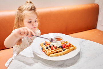 Happy 3 year old girl eat. Breakfast in cafe. Classic Viennese waffles with ice cream, berries and...