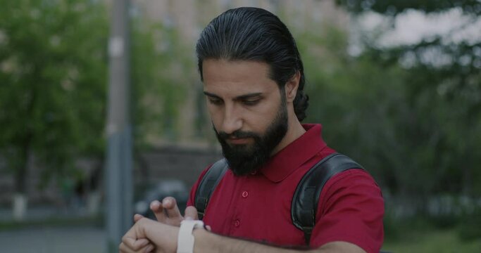 Portrait of Middle Eastern man using smart watch touching device standing in city street. Modern technology and contemporary gadgets concept.