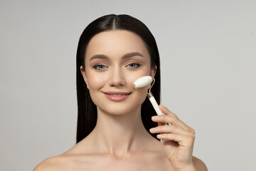 Fototapeta premium A beautiful girl does facial massage with a roller, on a gray background