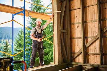 Carpenter constructing wooden frame two-story house near the forest. Portrait of bearded man...