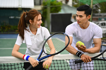 Experienced male tennis coach giving instructions to his student, standing by net at the outdoor...