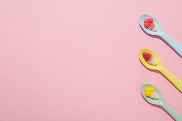 Jelly candies in spoons on pink background, space for text