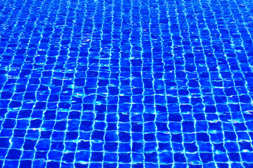 The blue tiles floor under the clear water in the swimming pool background, Swimming pool surface...