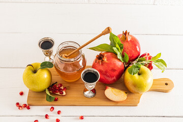 Beautiful still life with ripe pomegranates and apples, a glass silver of wine and a bowl of honey. White background. The concept of Rosh Hashanah.