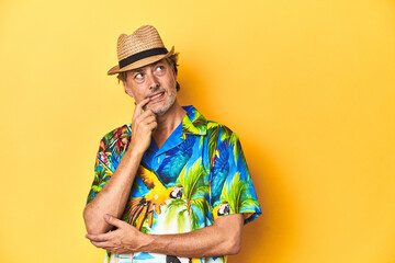 Middle-aged man in Hawaiian shirt and straw hat Middle-aged man in Hawaiian shirt and straw hatrelaxed thinking about something looking at a copy space.