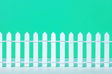 Wooden toy white picket fence on green background. Small painted simple wood decorative fencing