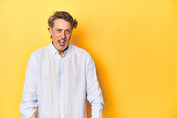 Middle-aged man posing on a yellow backdrop shouting very angry, rage concept, frustrated.