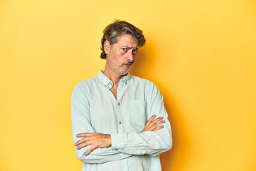 Middle-aged man posing on a yellow backdrop suspicious, uncertain, examining you.