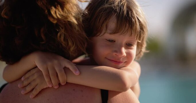 Close up happy little child hugging mom under scorching summer hot sun. Child hugs mother, smiling and laughing, mother kisses child. Hugs of son and mother on vacation. View from behind mother's back