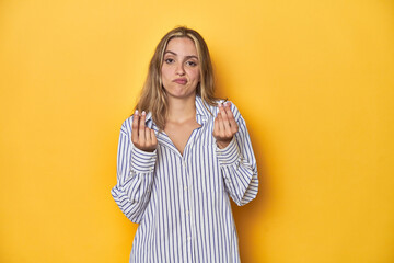 Young blonde Caucasian woman in a striped business shirt on a yellow background, showing that she...