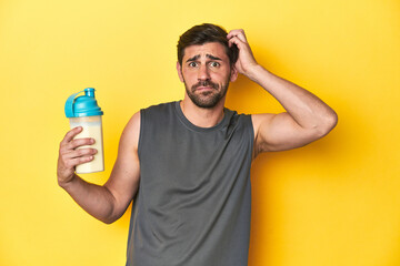 Fit man with protein shake, yellow studio background being shocked, she has remembered important...
