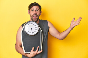 Athletic man with scale, on a yellow studio backdrop receiving a pleasant surprise, excited and...