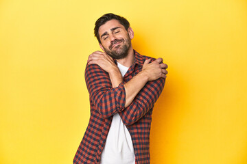 Fototapeta premium Caucasian man in red checkered shirt, yellow backdrop hugs, smiling carefree and happy.
