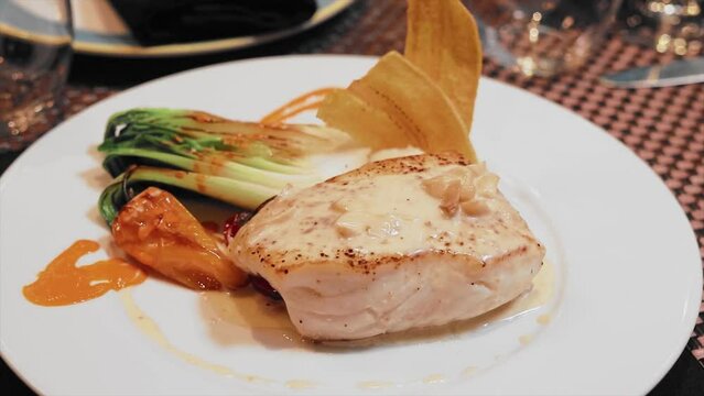 Close up Plate of halibut with garlic sauce on the table with crystal glasses of wine in a fancy restaurant.