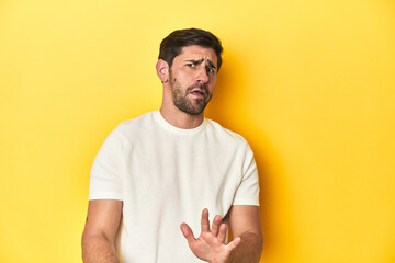 Caucasian man in white t-shirt on yellow studio background rejecting someone showing a gesture of disgust.