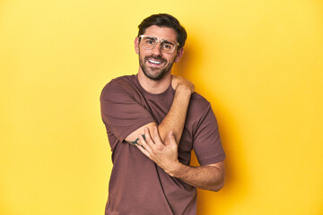 Man stretching arm on a yellow studio background.