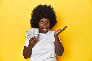 African-American woman holding cash, displaying wealth surprised and shocked.