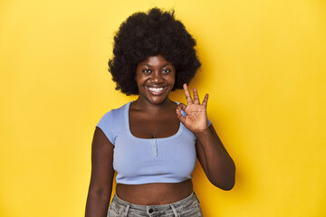 Fototapeta na wymiar African-American woman with afro, studio yellow background cheerful and confident showing ok gesture.