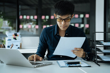 Asian business man working at office with laptop and documents on his desk, financial adviser analyzing data.