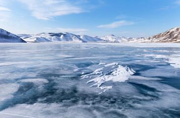 Beautiful winter landscape of the frozen Baikal Lake on sunny cold day. Snow-covered coastal hills and mountains surround the frozen shallow bay. Natural seasonal background, environment