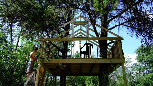 Men working on wall or siding of unfinished tree house and starting platform for zip line.