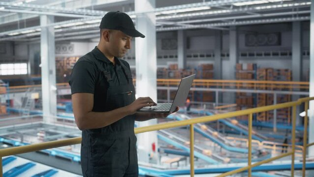 Logistics Transportation Warehouse Facility: Associate Worker Using Laptop in Retail Distrubution Center, Monitoring the Conveyors Loading Online Ordered Product Boxes for Delivery to Customers