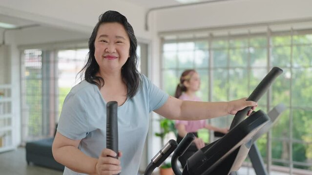 Close up smiling face of elderly women exercise on the machine in living room and looking at camera. Elderly lifestyle and concept