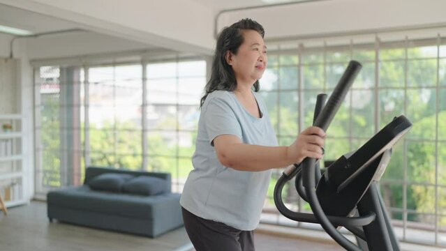 Happy asian senior women exercise on the machine in living room. Elderly women enjoy working out at home. Elderly lifestyle, Wellbeing concept