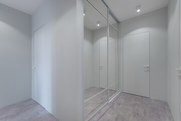 Modern design of the hallway with white decor of walls and doors. Built-in wardrobe with sliding mirror doors.