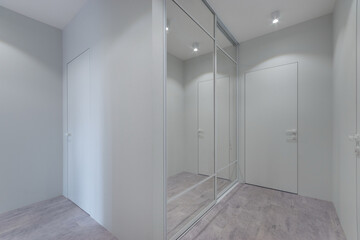 Modern design of the hallway with white decor of walls and doors. Built-in wardrobe with sliding...