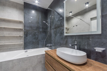 The bathroom is decorated with gray tiles. Shelves over the bathroom, a square mirror .over the sink bowl.