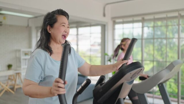 Happy elderly women and daughter enjoy exercising on the machine in living room at home on weekend. Elderly lifestyle, Famity activity