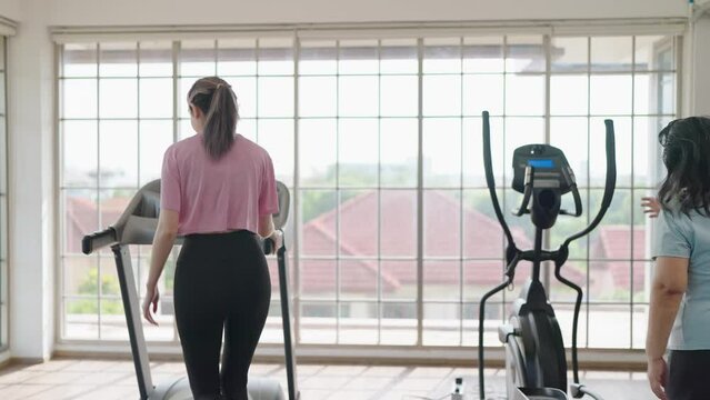 Back view of elderly women and daughter give high five before exercising on the machine together in living room at home. Elderly lifestyle, Famity activity concept