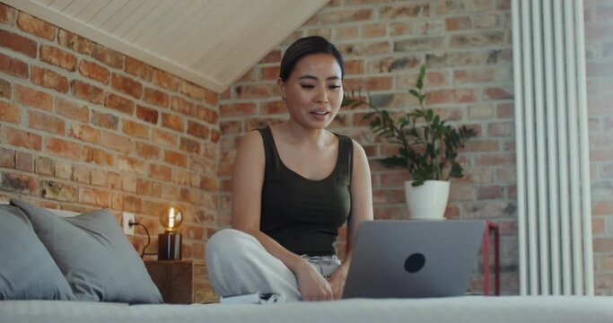 A young pregnant woman shows ultrasound images talking on a video call on a laptop while sitting on a bed at home