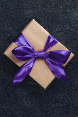 A gift in a rectangular box wrapped in craft paper. A present for a man tied with a purple bow.