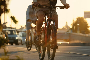 Two friends are riding bicycles along a cycle path next to a city road in the backlight from the...