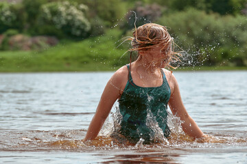 A child of 10-12 years old in a bathing suit swims cheerfully in the river in nature. Girl jumping and splashing with water on a hot summer day, close-up.