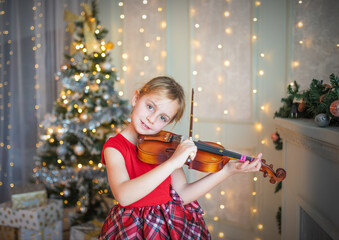 Young girl playing violin in front of christmas tree.