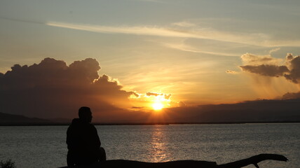 Fototapeta premium Silhouette of a man sitting on the lake and watching the sunset