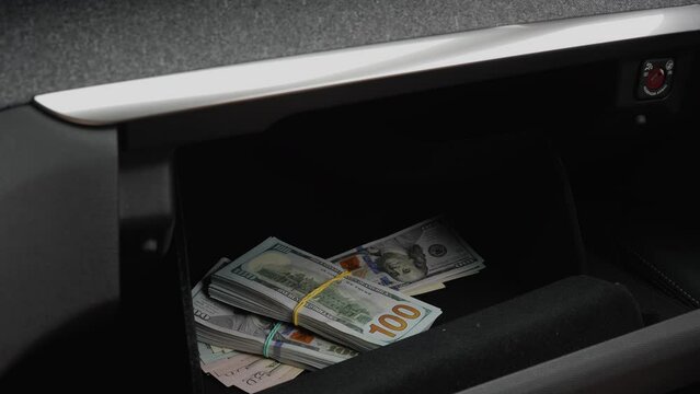 Caucasian male pulling out concealed handgun and a large sum of money from car glove box compartment. Close up shot