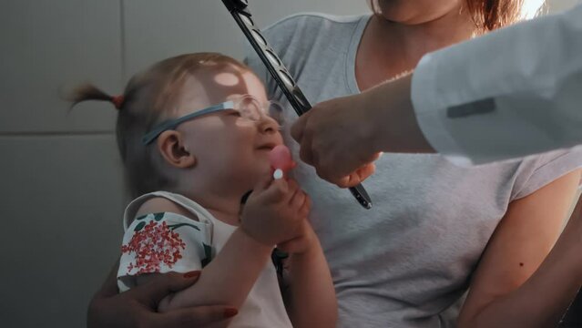 Diagnostic procedure skiascopy with pediatric ophthalmologist. Optometrist illuminates pupil of eye with mirror of ophthalmoscope, skiascopic ruler. Checking vision of little girl kid with eye disease