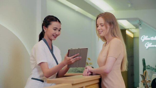 Medium shot of administrator offering procedure to client showing information on digital tablet at spa salon