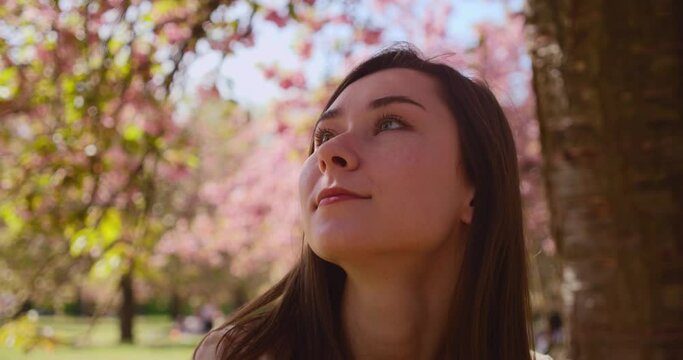 Closeup of an asian girl in the Parc de Sceaux (Paris, France). On the blurred backroung there are sakura trees in bloom. Bright slow mo shot. Spring time