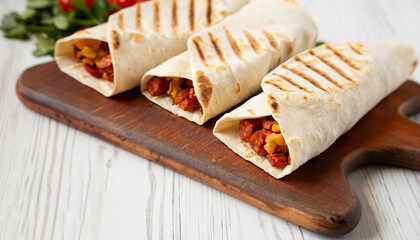 Homemade chorizo breakfast burritos on a rustic wooden board on a white wooden surface, low angle view. Close-up.