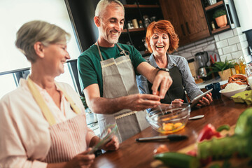 Group of senior friends at dinner party at home, cooking.